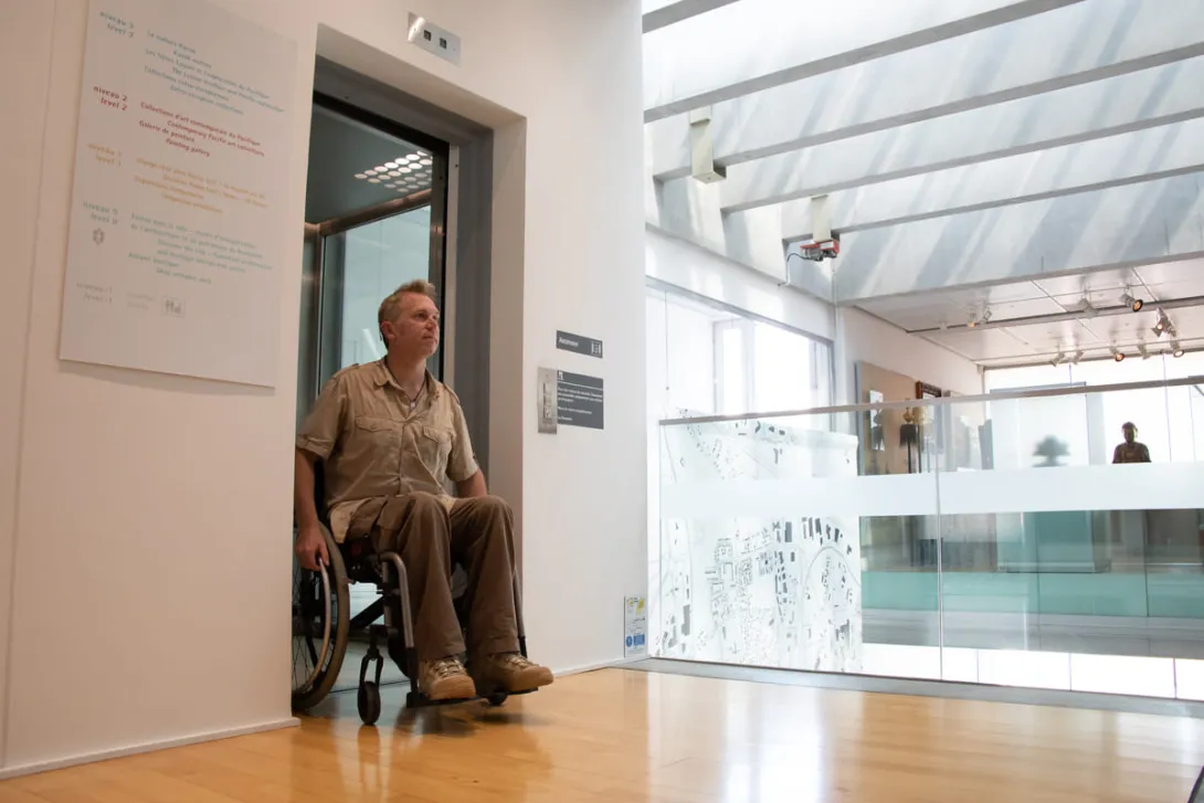 Une personne en fauteuil roulant sort d'un ascenceur